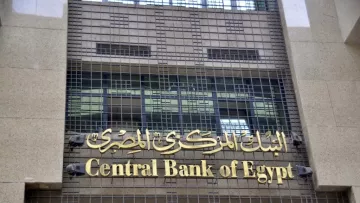 L'image montre la façade d'un bâtiment moderne, probablement celle de la Banque centrale d'Égypte. On peut voir le nom de l'institution écrit en arabe et en anglais, avec un design sobre et élégant. La structure est faite de granite et présente des grilles métalliques sur les fenêtres, ce qui donne une impression de sécurité et de solidité.