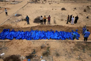 Des corps enveloppés de bleu sont placés dans une fosse, entourés de personnes en deuil.