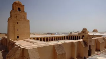 Edificio storico con torri e architettura in sabbia chiara, sole intenso.
