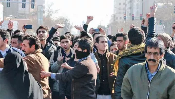 L'image montre une foule de personnes rassemblées dans une rue. Les individus semblent engagés dans une forme de manifestation ou de rassemblement collectif. Certains lèvent les mains ou filment avec des téléphones, tandis que d'autres ont des expressions préoccupées ou déterminées. On peut voir une diversité d'habillements, y compris des vêtements traditionnels, et un mélange de genres parmi les participants. L'ambiance générale semble être celle de l'enthousiasme ou de la passion pour une cause commune.