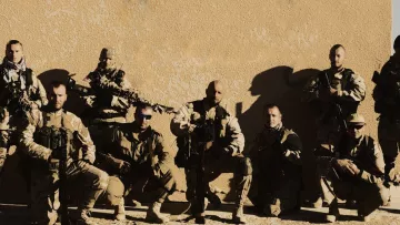الصورة تظهر مجموعة من الجنود أو أفراد القوات المسلحة، يقفون معًا في وضعية تعكس القوة والانضباط. يرتدون زيًا عسكريًا ويحملون أسلحة، ويظهرون بمظهر جاد. الخلفية تبدو بسيطة، مما يركز الانتباه على المجموعة. تعكس الصورة روح الفريق والتضامن بين الأفراد.