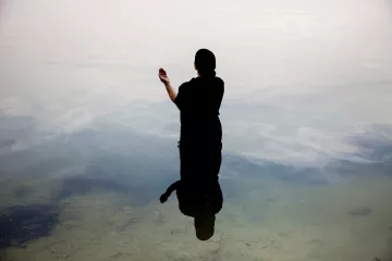 Une silhouette noire se tient dans l'eau calme, reflet visible à la surface.