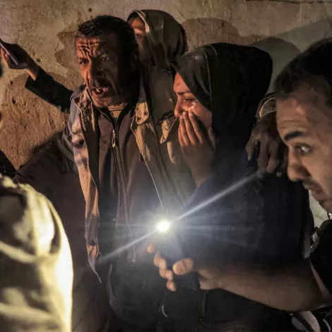 A group of people in a dim space, some worried, holding cell phone lights in tense expressions.
