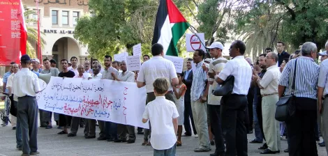 Un gruppo di persone in protesta con bandiera palestinese e striscioni.