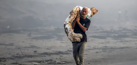 Un uomo attraversa un paesaggio desolato, portando un oggetto pesante sulle spalle.