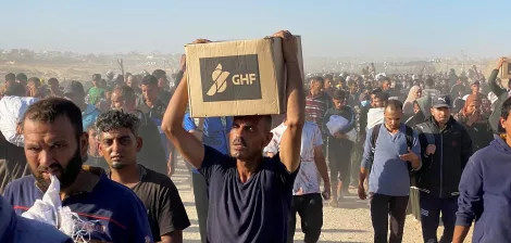 Un groupe de personnes marchent, portant des cartons dans un environnement poussiéreux.