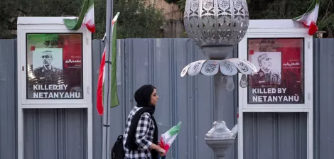 Deux affiches de victimes avec le texte "Killed by Netanyahu", une femme passe avec un drapeau.