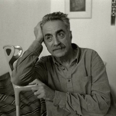 Homme pensif, assis, avec une canne, dans une pièce simple et lumineuse.