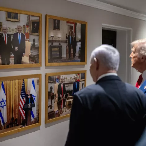 Des hommes politiques regardent des photos accrochées au mur, représentant des rencontres officielles.