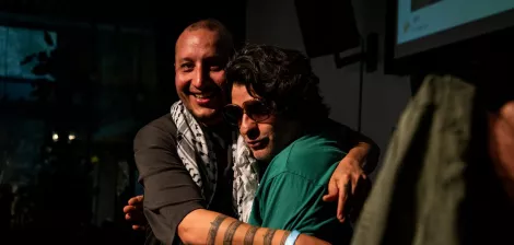 Deux hommes s'étreignent, souriants, avec des déguisements et un ambiance chaleureuse.