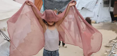 Enfant joyeux tenant un tissu léger, jouant près de tentes.
