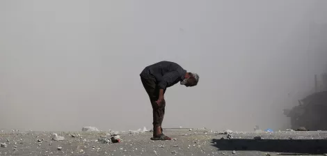 Un homme âgé se penche, entouré de débris et de poussière.