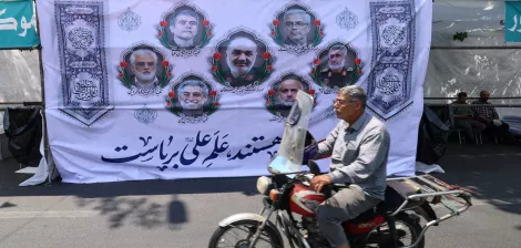 Un homme à moto passe devant une grande affiche avec des portraits et des motifs décoratifs.