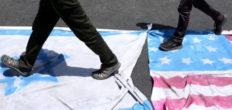 Deux personnes marchent sur des drapeaux américains et cubains étalés au sol.