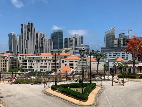 صورة لمدينة حديثة، مباني مرتفعة، سماء زرقاء وأشجار. يبدو النشاط العمراني واضحًا.