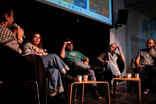 Quatre personnes assises discutent sur scène, avec des gobelets et un écran en arrière-plan.