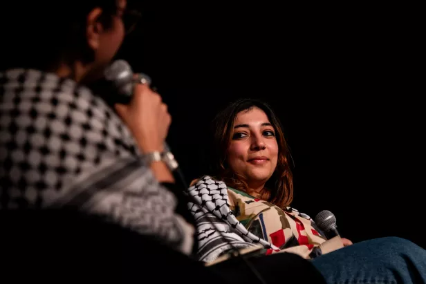 Deux femmes en discussion sur scène, l'une souriant à l'autre, dans une ambiance sombre.
