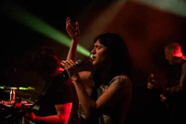 Une chanteuse passionnée chantant sur scène, entourée de musiciens. Lumières colorées.