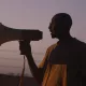 Un homme en silhouette tenant un mégaphone au crépuscule.