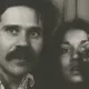 Un homme avec une moustache et une femme montrant un doigt vers l'objectif.
