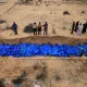 Des corps enveloppés de bleu sont placés dans une fosse, entourés de personnes en deuil.