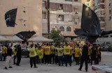 Un groupe de personnes brandissant des drapeaux noirs et jaunes dans une cour.