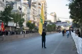 Une personne tient un drapeau sur une rue, entourée de bâtiments et de manifestants.