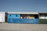 Bâtiment en tôle bleue avec vêtements suspendus et murs colorés en arrière-plan.