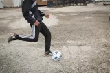 Un jeune garçon dribble un ballon de foot sur un terrain gravelé.
