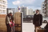 Deux hommes et une fille souriante devant un bâtiment, un autre homme les observe. 