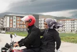 Un homme en moto avec une passagère, tous deux portant des vêtements sombres et un casque.