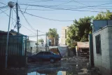 Une rue avec des fils électriques, une voiture bleue et des bâtiments en arrière-plan.