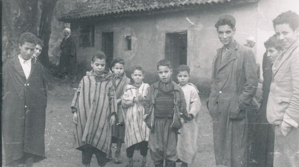 Groupe d'enfants en tenue traditionnelle, devant une maison, ambiance d'époque.
