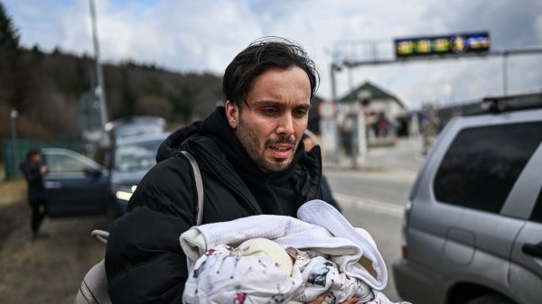 Un homme porte un bébé dans les bras, visiblement bouleversé, près d'une route.