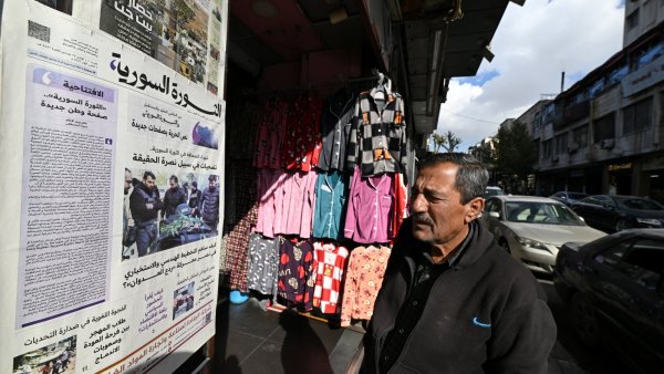 Un homme regarde un journal affiché devant un magasin de vêtements colorés.