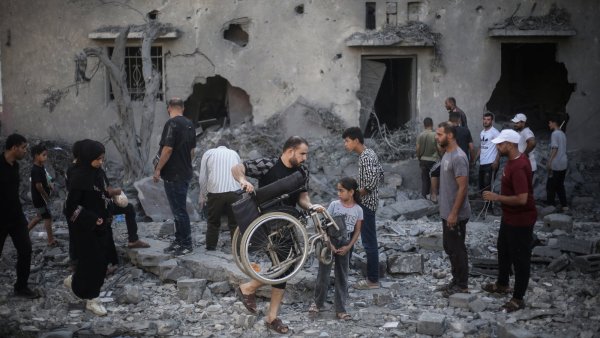 Des personnes dans les décombres, un homme porte un fauteuil roulant, scène de destruction.