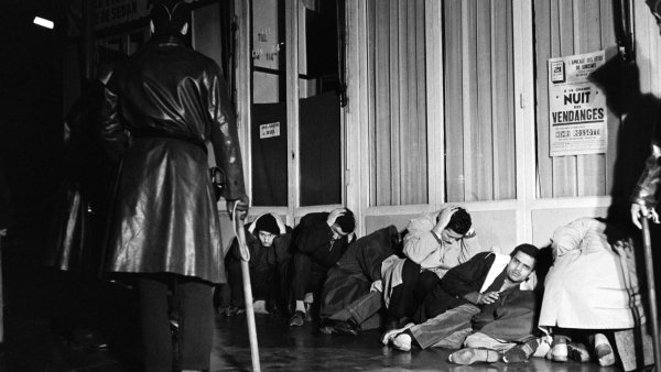 Des personnes assises sur le sol, couvertes, sous une lumière tamisée, semblant anxieuses.
