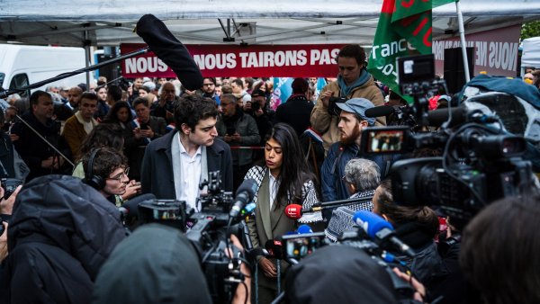 Une foule rassemblée autour de journalistes et de manifestants sous un chapiteau.