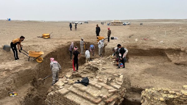 Des archéologues fouillent un site désertique, entourés de terre et de briques anciennes.