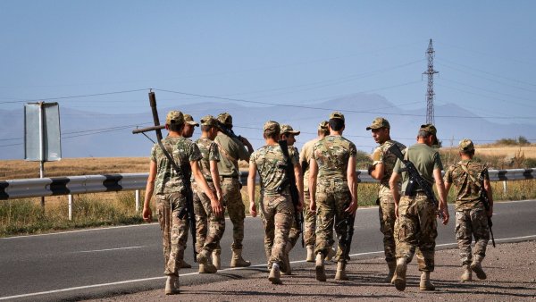 Des soldats marchent en groupe sur une route, avec des montagnes en arrière-plan.