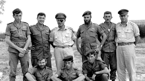 Groupe de militaires en uniforme, posant ensemble en extérieur, sourires et camaraderie.