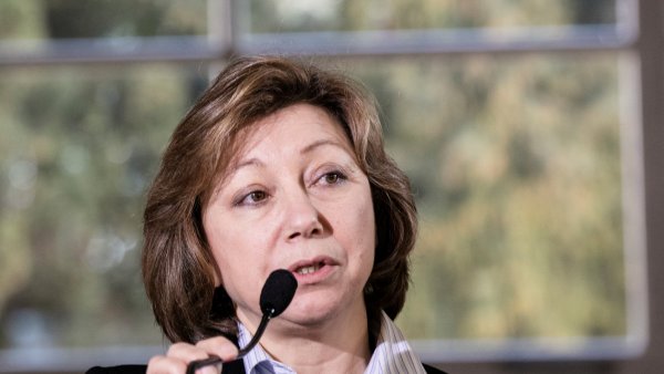 Femme brune parlant au micro, en arrière-plan, un flou de verdure.