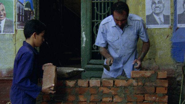 Un homme construit un mur en briques avec un jeune garçon à ses côtés.