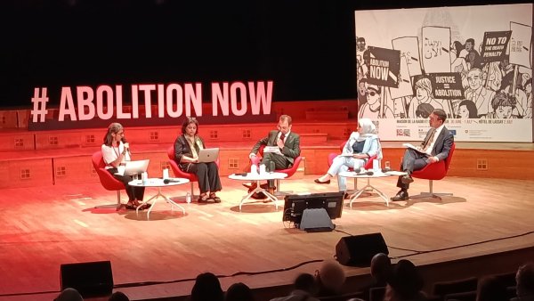 Des intervenants discutent sur scène, avec un public attentif et des affiches en arrière-plan.