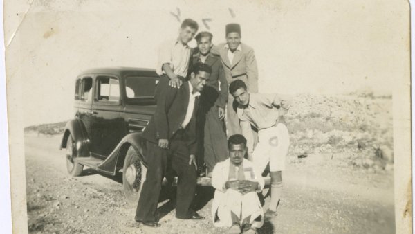 Groupe de six hommes posant près d'une voiture ancienne sur une route.