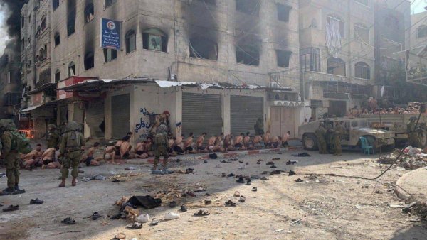 Scène de rue sombre avec des personnes assises et des soldats armés. Atmosphère tendue.