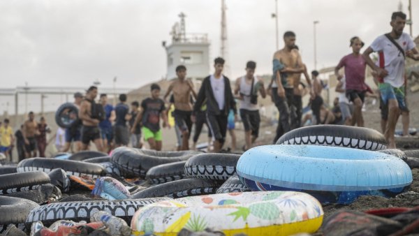 Des personnes marchent sur une plage, entourées de bouées colorées abandonnées.