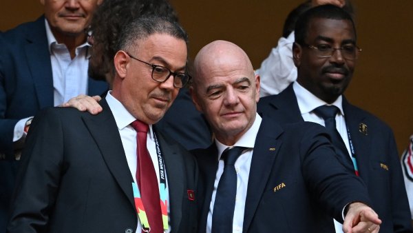 Deux hommes en costume sourient, discutent et montrent un point du doigt, ambiance conviviale.