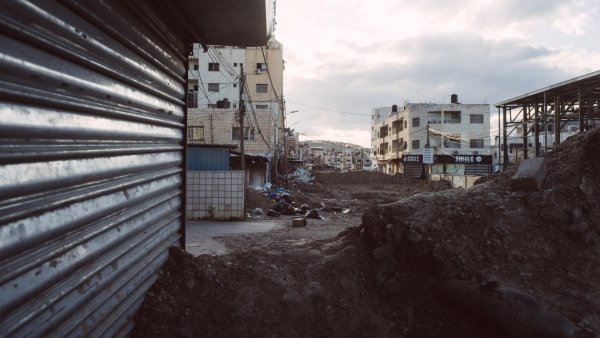 Vue d'une rue déserte avec des bâtiments et des gravats, ciel nuageux en arrière-plan.