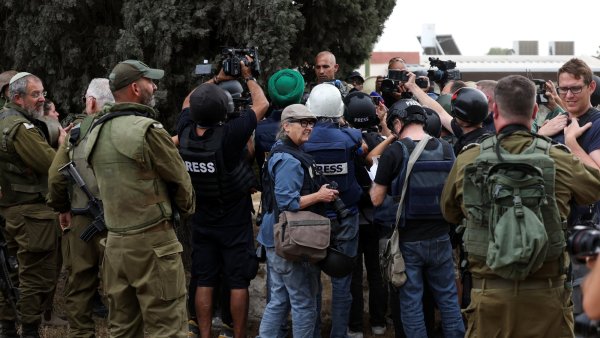 Groupe de journalistes entouré de soldats, ambiance tendue et présence de caméras.